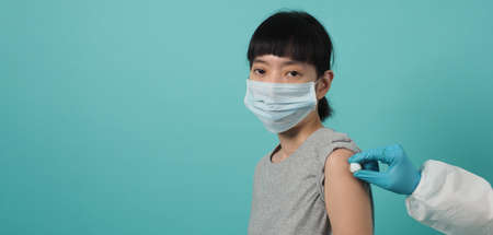Vaccine Concept. Woman waiting for coronavirus vaccine injection by doctor. Asian woman with medical mask open shoulder and upper arm on blue green background. Waiting for vaccination.の写真素材