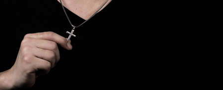 Praying with a rosary. hand of Catholic man with rosary on black background. Hands holding a silver...