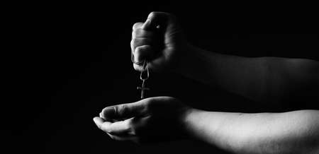 Praying with a rosary. hand of Catholic man with rosary on black background. Hands holding a silver...