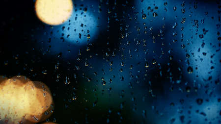 Rain drop on window at night. Condominium or apartment living room window on rainy season night in Bangkok Thailand. Outside window is blurred bokeh of raining city light and natural tree and sky.の写真素材