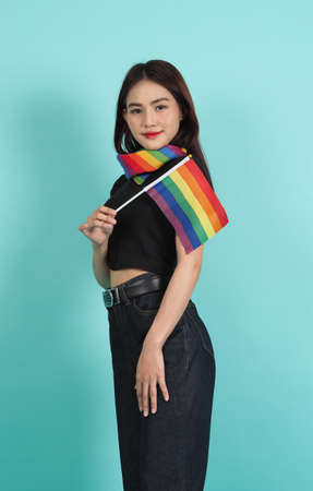 LGBTQ girl and pride flag. Sexy Lesbian girl and LGBTQ flag standing. blue green background. Asian LGBTQ woman with rainbow scarf on neck. Energetic cheerful. LGBTQ concept. LGBTQA+ Pride Month.の写真素材