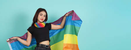 LGBTQ girl and pride flag. Sexy Lesbian girl and LGBTQ flag standing. blue green background. Asian LGBTQ woman with rainbow scarf on neck. Energetic cheerful. LGBTQ concept. LGBTQA+ Pride Month.の写真素材