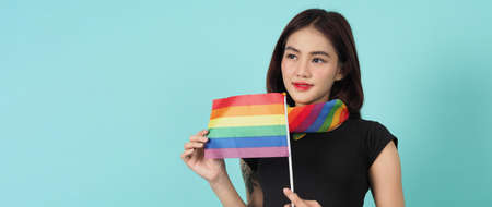 LGBTQ girl and pride flag. Sexy Lesbian girl and LGBTQ flag standing. blue green background. Asian LGBTQ woman with rainbow scarf on neck. Energetic cheerful. LGBTQ concept. LGBTQA+ Pride Month.の写真素材