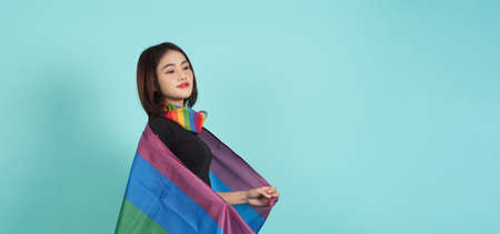 LGBTQ girl and pride flag. Sexy Lesbian girl and LGBTQ flag standing. blue green background. Asian LGBTQ woman with rainbow scarf on neck. Energetic cheerful. LGBTQ concept. LGBTQA+ Pride Month.の写真素材
