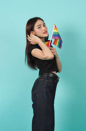 LGBTQ girl and pride flag. Sexy Lesbian girl and LGBTQ flag standing. blue green background. Asian LGBTQ woman with rainbow scarf on neck. Energetic cheerful. LGBTQ concept. LGBTQA+ Pride Month.の写真素材
