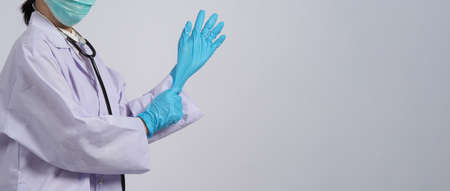 Wearing gloves. Asian doctor wear blue rubber nitrile hands glove. Doc with a mask putting on...