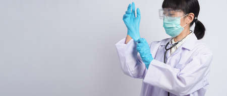 Wearing gloves. Asian doctor wear blue rubber nitrile hands glove. Doc with a mask putting on gloves. isolated white background copy space. Health care protection coronovirus pandemic concept.の写真素材