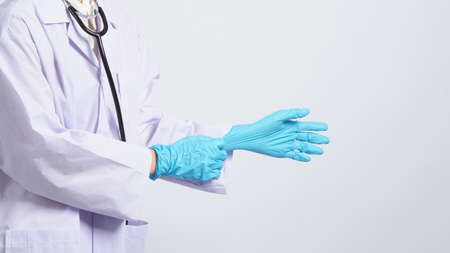 Wearing gloves. Asian doctor wear blue rubber nitrile hands glove. Doc with a mask putting on gloves. isolated white background copy space. Health care protection coronovirus pandemic concept.の写真素材