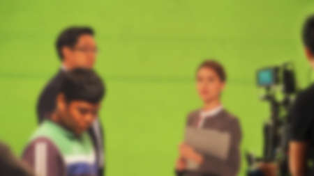 Blurry images of making TV commercial movie video in big green screen background. Film crew team working with actor. Recording by professional digital camera and lighting set. film behind the scenesの写真素材