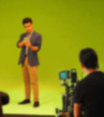 Blurry images of making TV commercial movie video in big green screen background. Film crew team working with actor. Recording by professional digital camera and lighting set. film behind the scenesの写真素材