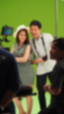 Blurry images of making TV commercial movie video in big green screen background. Film crew team working with actor. Recording by professional digital camera and lighting set. film behind the scenesの写真素材
