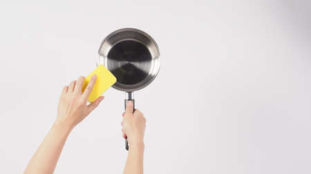 Pot cleaning. Man hand on white background cleaning the non stick pot with handy dish washing sponge which yellow color on the soft side and green on hard side for hygiene after cook. Electric pot.の写真素材