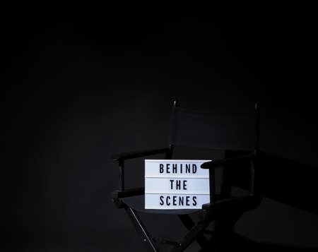 Director chair with behind the scene banner light box. Letterboard text Lightbox or Cinema Light box. Movie clapperboard and Director chair. Black Background. Represent video behind the scenes is on.の写真素材