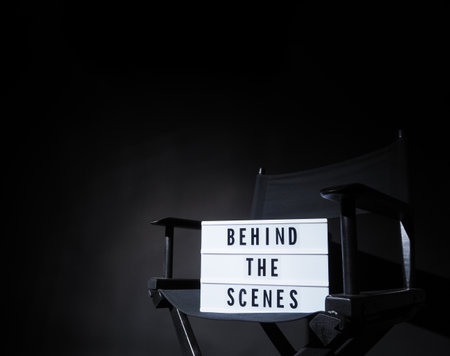 Director chair with behind the scene banner light box. Letterboard text Lightbox or Cinema Light box. Movie clapperboard and Director chair. Black Background. Represent video behind the scenes is on.の写真素材