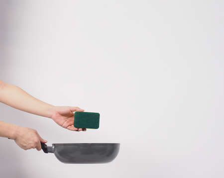 Cleaning Electric non stick pan. Hand on white background cleaning the non stick pan with handy dish washing sponge which yellow color on the soft side and green on hard side for hygiene after cook.の写真素材