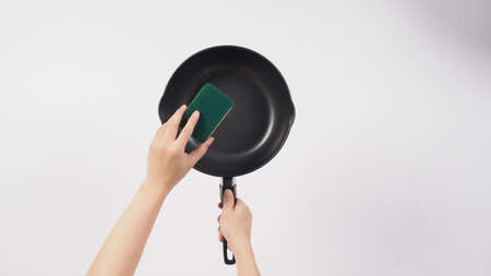 Cleaning Electric non stick pan. Hand on white background cleaning the non stick pan with handy dish washing sponge which yellow color on the soft side and green on hard side for hygiene after cook.の写真素材