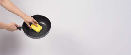 Cleaning Electric non stick pan. Hand on white background cleaning the non stick pan with handy dish washing sponge which yellow color on the soft side and green on hard side for hygiene after cook.の写真素材