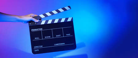 Blurry images of movie slate or clapper board. Hand holds empty film making clapperboard on color...