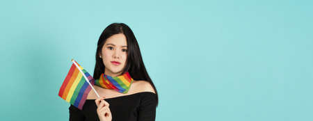 LGBTQ woman holding pride flag standing against a blue green background. Asian LGBTQ woman with rainbow scarf on neck. look smart bright and energetic cheerful. LGBTQ diversity pride concept.の写真素材