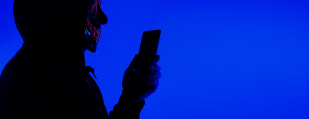 Digital security Concept. Anonymous hacker with mask holding smartphone hacked. Personal and Cyber...