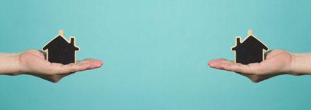 Small wood house in hands represent concepts such as home care family love real estate housing shelter insurance and mortgage. Hands holding small model house isolated on blue green studio background.の写真素材