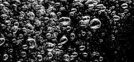Soda water bubbles splashing underwater against black background. Cola liquid texture that fizzing and floating up to surface like a explosion in under water for refreshing carbonate drink concept.の写真素材