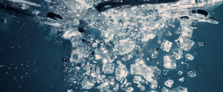 Water splashing and ice cube. Ice splashing into a glass of water. Underwater pouring ice cubes falling into clear watering background. Refreshing chill drinking. Ices in a glass with blue backgroundの写真素材