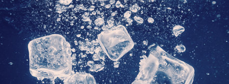 Water splashing and ice cube. Ice splashing into a glass of water. Underwater pouring ice cubes falling into clear watering background. Refreshing chill drinking. Ices in a glass with blue backgroundの写真素材