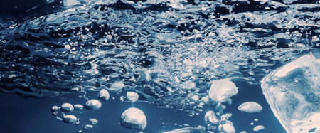 Water splashing and ice cube. Ice splashing into a glass of water. Underwater pouring ice cubes falling into clear watering background. Refreshing chill drinking. Ices in a glass with blue backgroundの写真素材