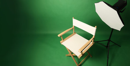 Photo studio with green screen background and wooden stool against professional lighting equipment. Interior of photo studio with professional lighting equipment and director chair with green backdropの写真素材