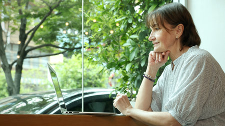 Senior and Technology. Middle aged or senior woman enjoys remote work and online communication technology using various digital devices laptop tablet or smartphone in greeny filled cafe natural lightの写真素材