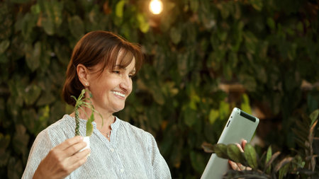 Senior and Technology. Middle aged or senior woman enjoys remote work and online communication technology using various digital devices laptop tablet or smartphone in greeny filled cafe natural lightの写真素材