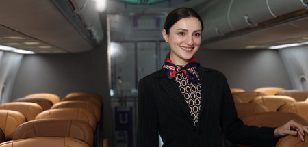 Flight attendant or Air Hostess. A friendly flight attendant stand confidently inside an airplane cabin. Professional hospitality and elegant uniform. Aviation service travel airline Flight attendant.の写真素材