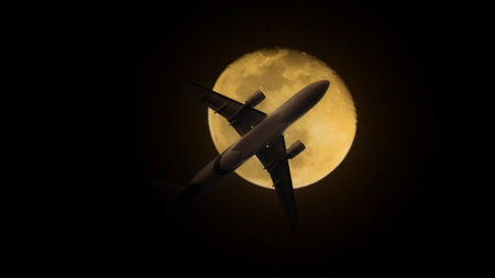 Airplane in the sky. Airplane in flight at sunset or evening sky. Commercial airliner silhouette in the colorful evening or night moon skies. Aircraft symbol of travel adventure global connectivity.の写真素材