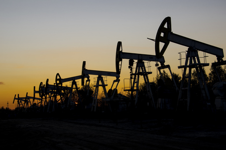 Pump jacks silhouettes during sunset on the oilfield. Oil and gas concept.の写真素材