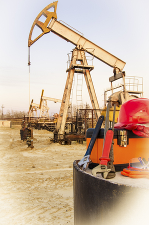 Tool box, helmet and wrenches on the background of blurry pump jack. Oil and gas concept. Toned.の写真素材