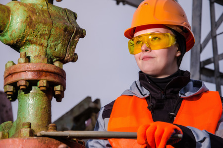 Woman engineer in the oil field repairing wellhead with the wrench wearing orange helmet and work clothes. Oil and gas concept.の写真素材