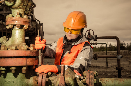 Woman engineer in the oil field repairing wellhead with the wrench wearing orange helmet and work clothes. Oil and gas concept. Toned.の写真素材