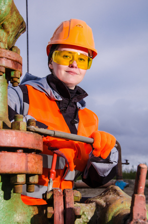Woman engineer in the oil field repairing wellhead with the wrench wearing orange helmet and work clothes. Oil and gas concept.の写真素材