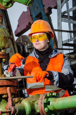 Woman engineer in the oil field repairing wellhead with the wrench wearing orange helmet and work clothes. Oil and gas concept.の写真素材