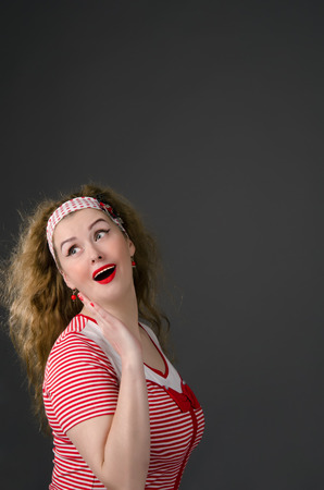 Beautiful young pin-up woman wearing red cloths with radiant red lipstick. Dark background.の写真素材