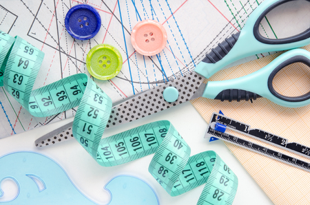 Sewing kit on the background of the pattern and scaled paper. Colorful set consisting of scissors, cutter?s ruler, buttons and measuring tape.の写真素材