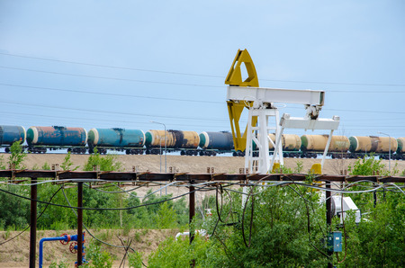 Pump jack, well head and pipeline on the background of moving tank train. Oil and gas concept.の写真素材