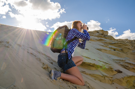 Young beautiful woman backpacker traveling and making pictures in the desert. Sandy dunes and blue sky on sunny summer day. Travel, adventure, freedom concept. Toned.の写真素材