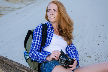 Young beautiful woman backpacker traveling in the desert and making pictures with vintage film camera. Sandy dunes background. Travel, adventure, freedom concept. Toned.の写真素材