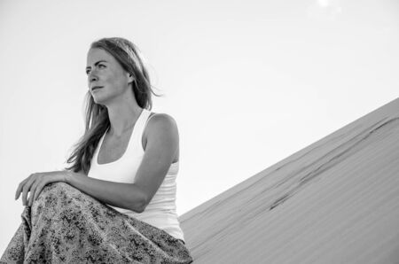 Young beautiful woman traveling in the desert. Yoga style dress. Sandy dunes background. Travel, meditation, freedom, relaxation concept. Black and white shot.の写真素材