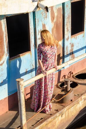 Young beautiful girl wearing long dress on the the background of old ship.の写真素材