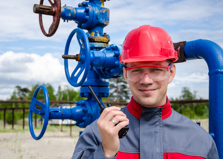 Worker near well head valve holding radio and wearing red helmet in the oilfield. Oil and gas concept.の写真素材