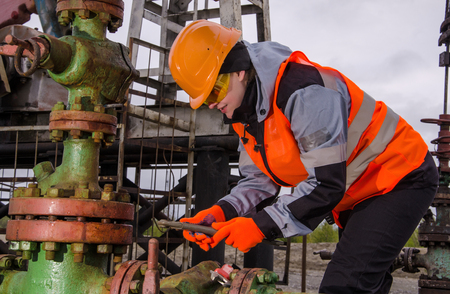 Woman engineer in the oil field repairing wellhead with the wrench wearing orange helmet and work clothes. Oil and gas concept.の写真素材