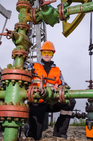Woman engineer in the oil field repairing wellhead with the wrench wearing orange helmet and work clothes. Pump jack background. Oil and gas concept.の写真素材